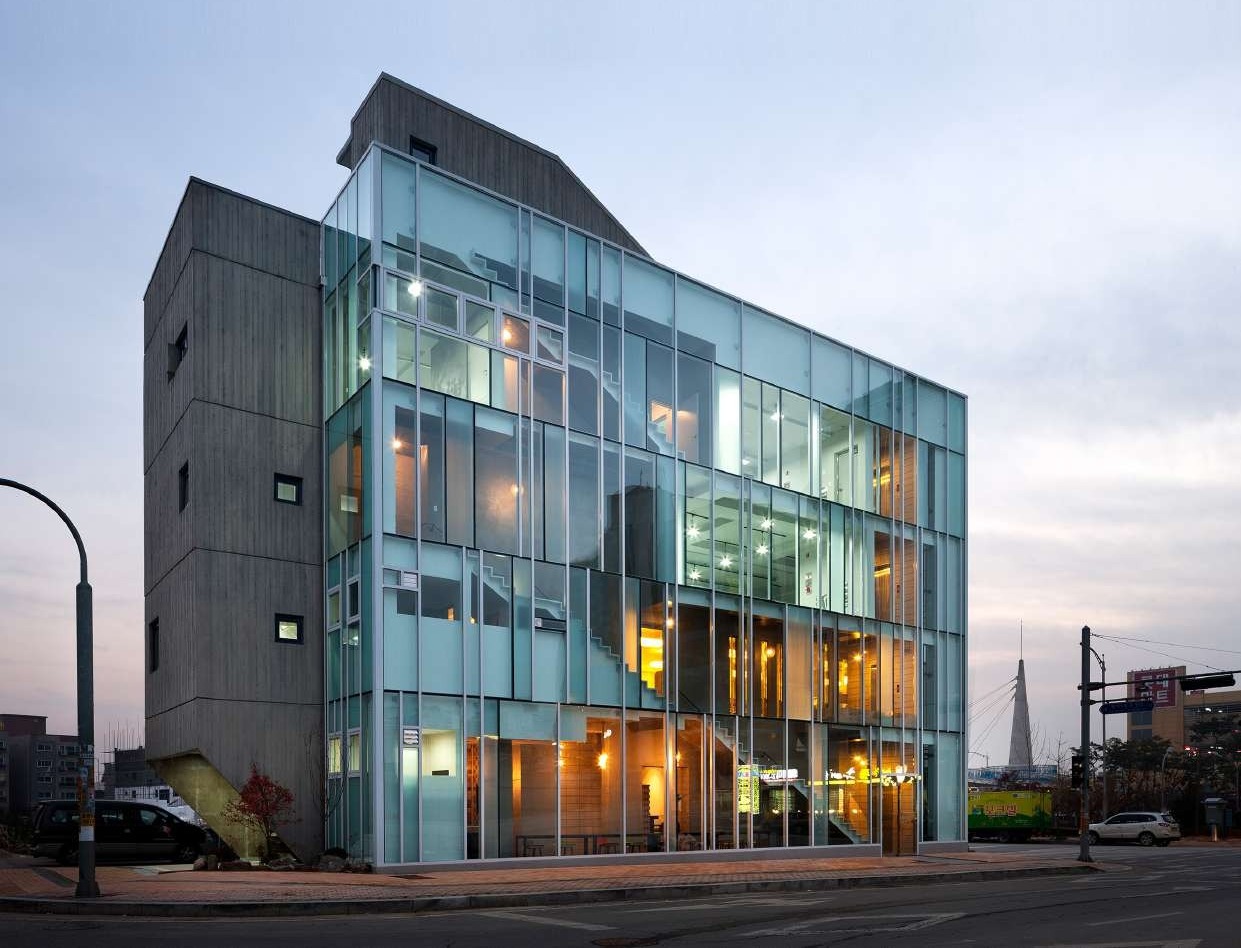 Glazed corner building lit from within at dusk on an urban street